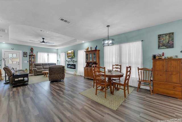 dining area with dark hardwood / wood-style floors, ceiling fan with notable chandelier, and a tray ceiling