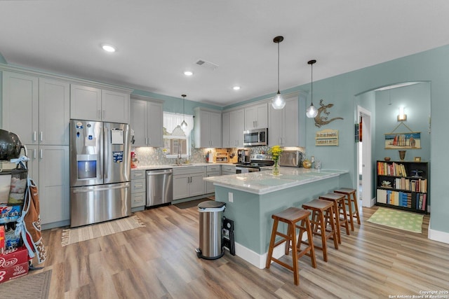 kitchen with a breakfast bar, sink, decorative light fixtures, kitchen peninsula, and stainless steel appliances