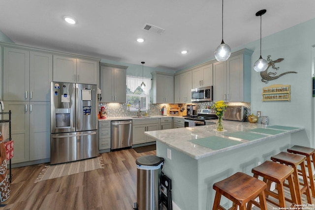 kitchen with a breakfast bar area, appliances with stainless steel finishes, gray cabinetry, decorative light fixtures, and kitchen peninsula