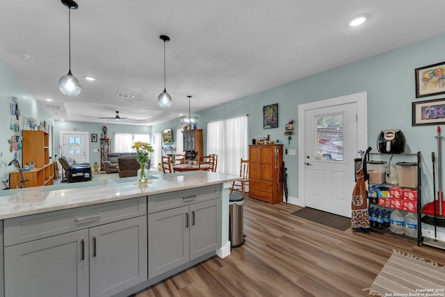 kitchen with wood-type flooring, light stone countertops, pendant lighting, and gray cabinetry