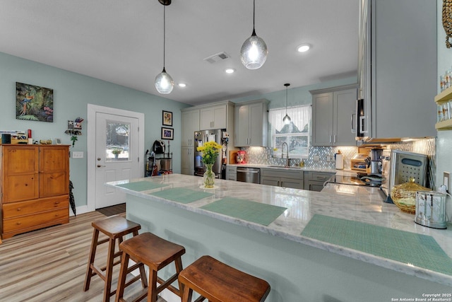 kitchen with a breakfast bar area, hanging light fixtures, appliances with stainless steel finishes, gray cabinets, and kitchen peninsula