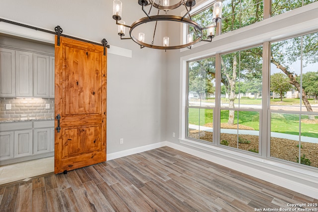 unfurnished dining area with a barn door, a chandelier, and hardwood / wood-style floors