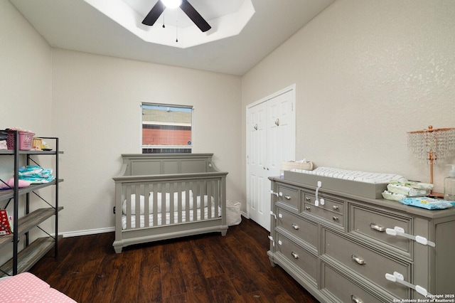 bedroom with dark hardwood / wood-style floors, a crib, ceiling fan, a raised ceiling, and a closet