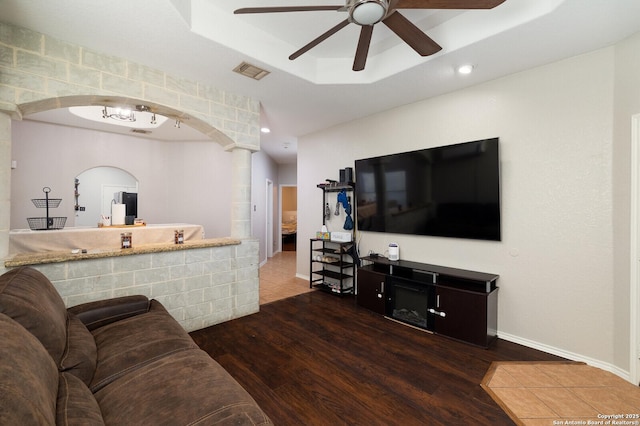 living room with dark wood-type flooring, ceiling fan, and a raised ceiling