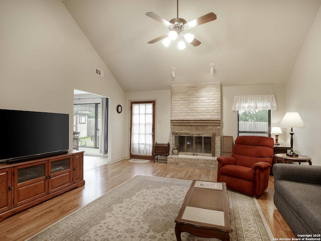 living room with a brick fireplace, light hardwood / wood-style flooring, high vaulted ceiling, and ceiling fan