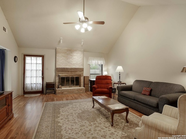 living room with ceiling fan, wood-type flooring, high vaulted ceiling, and a brick fireplace