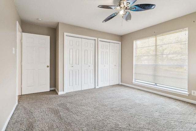 unfurnished bedroom featuring ceiling fan, carpet floors, and multiple closets