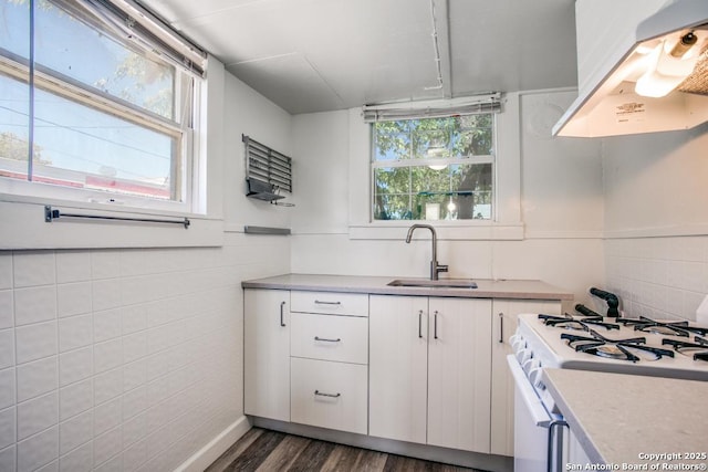 kitchen with sink, gas range gas stove, white cabinetry, tile walls, and exhaust hood