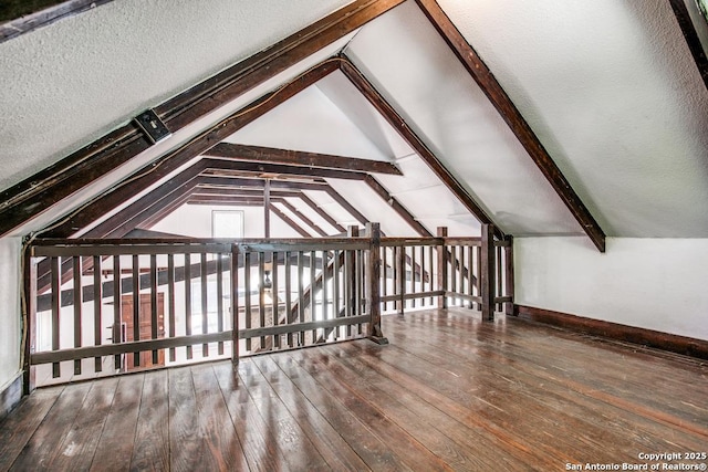 additional living space featuring wood-type flooring, a textured ceiling, and vaulted ceiling with beams