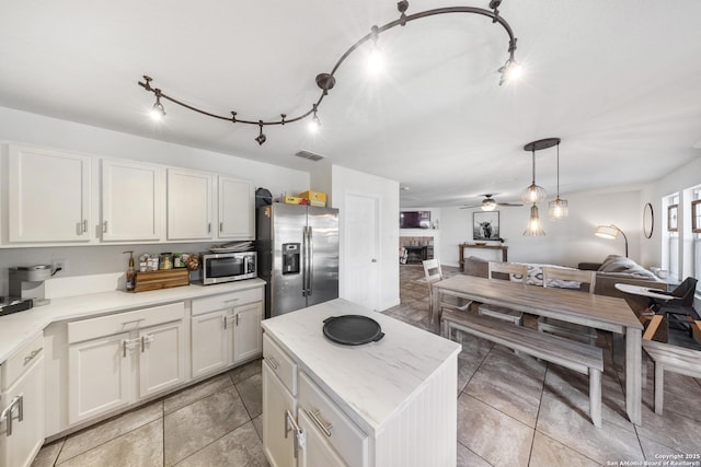 kitchen featuring appliances with stainless steel finishes, a fireplace, white cabinetry, a center island, and ceiling fan