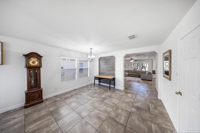 unfurnished living room featuring dark tile patterned flooring, ceiling fan with notable chandelier, and a textured ceiling