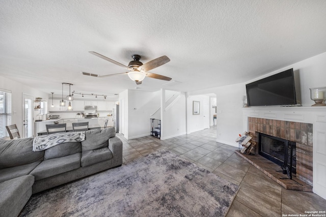 tiled living room featuring ceiling fan, a textured ceiling, and a fireplace