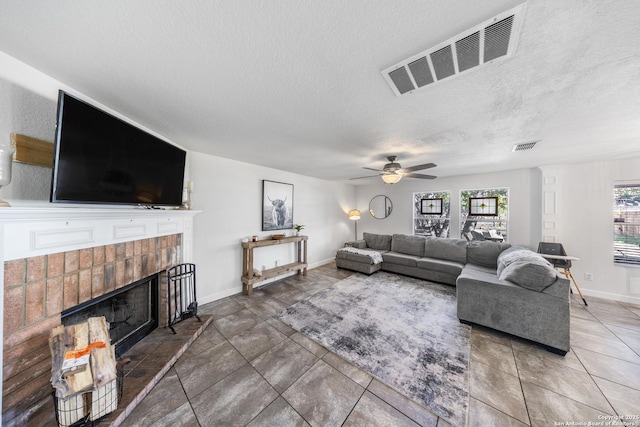 tiled living room with ceiling fan, a brick fireplace, and a textured ceiling