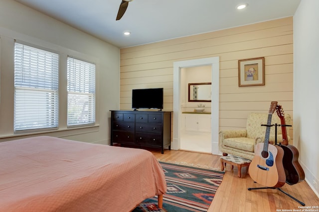 bedroom featuring ensuite bath, wood walls, ceiling fan, and light wood-type flooring