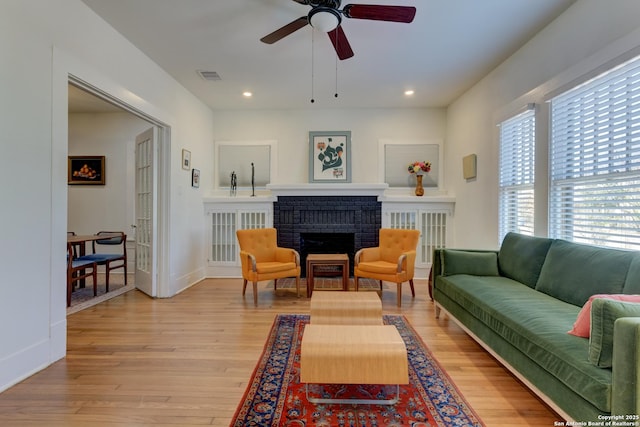 living room with a brick fireplace, ceiling fan, and light wood-type flooring