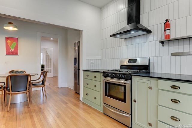 kitchen featuring wall chimney range hood, appliances with stainless steel finishes, tasteful backsplash, light hardwood / wood-style floors, and green cabinetry