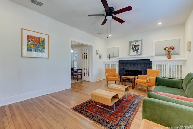 living room featuring ceiling fan, a brick fireplace, and light hardwood / wood-style flooring