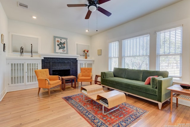 living room featuring hardwood / wood-style flooring, ceiling fan, and a brick fireplace