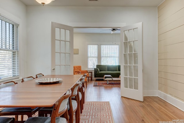 dining room featuring light hardwood / wood-style flooring, french doors, ceiling fan, and wood walls