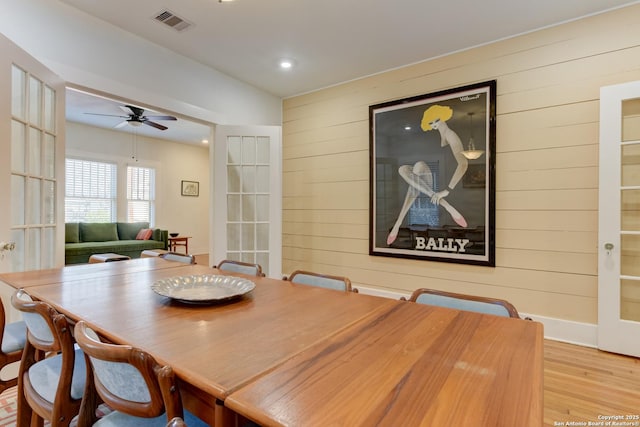 dining area with french doors, wood walls, ceiling fan, and light hardwood / wood-style flooring