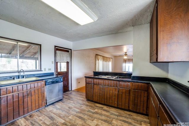 kitchen featuring a textured ceiling, wood finished floors, a sink, stainless steel dishwasher, and dark countertops