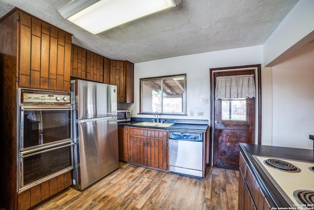 kitchen featuring dark countertops, stainless steel appliances, a textured ceiling, light wood-type flooring, and a sink