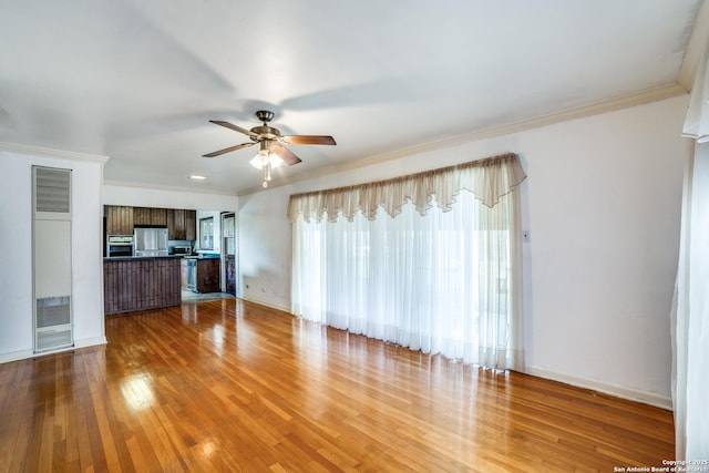 unfurnished living room with ceiling fan, ornamental molding, wood finished floors, and baseboards