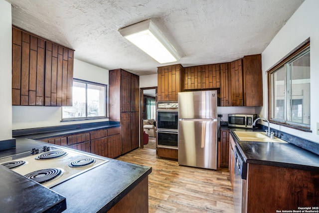 kitchen featuring dark countertops, light wood-style flooring, appliances with stainless steel finishes, and a sink