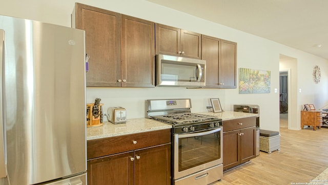 kitchen featuring appliances with stainless steel finishes, light stone counters, and light hardwood / wood-style floors