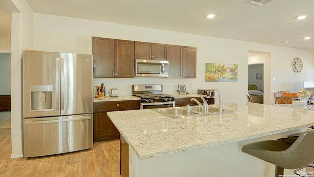 kitchen with sink, appliances with stainless steel finishes, an island with sink, light stone countertops, and light hardwood / wood-style floors