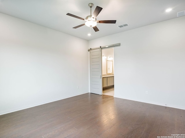 empty room with dark wood-type flooring, a barn door, and ceiling fan