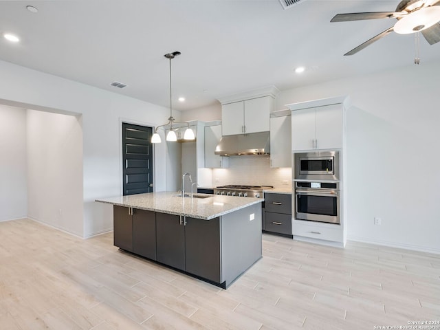 kitchen featuring decorative light fixtures, white cabinetry, sink, stainless steel appliances, and a center island with sink