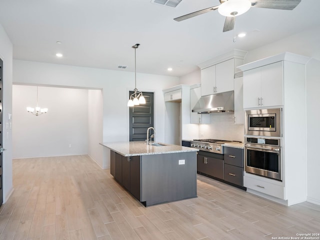 kitchen featuring sink, white cabinetry, light stone counters, a center island with sink, and appliances with stainless steel finishes