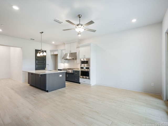 kitchen with appliances with stainless steel finishes, white cabinets, hanging light fixtures, a kitchen island with sink, and light hardwood / wood-style flooring