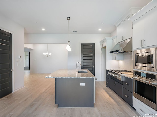 kitchen with sink, appliances with stainless steel finishes, an island with sink, white cabinets, and decorative light fixtures