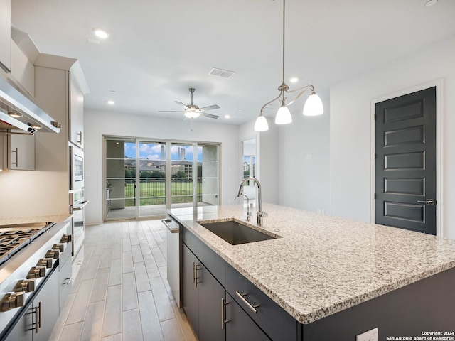 kitchen featuring pendant lighting, sink, appliances with stainless steel finishes, extractor fan, and an island with sink