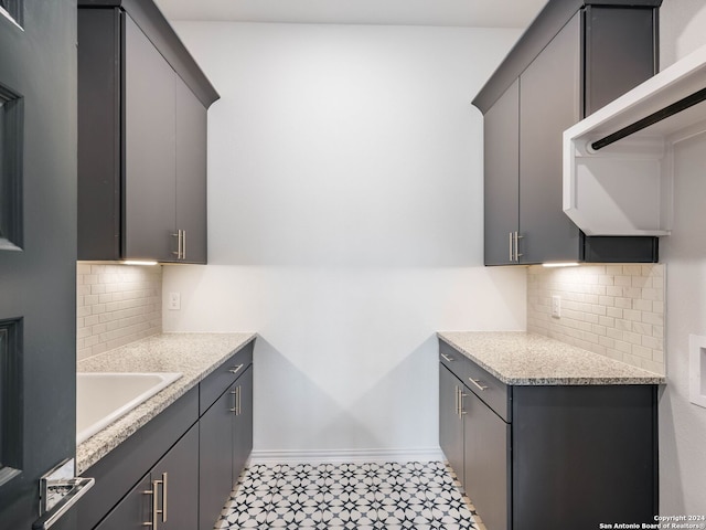 kitchen with gray cabinets, sink, light stone counters, and decorative backsplash