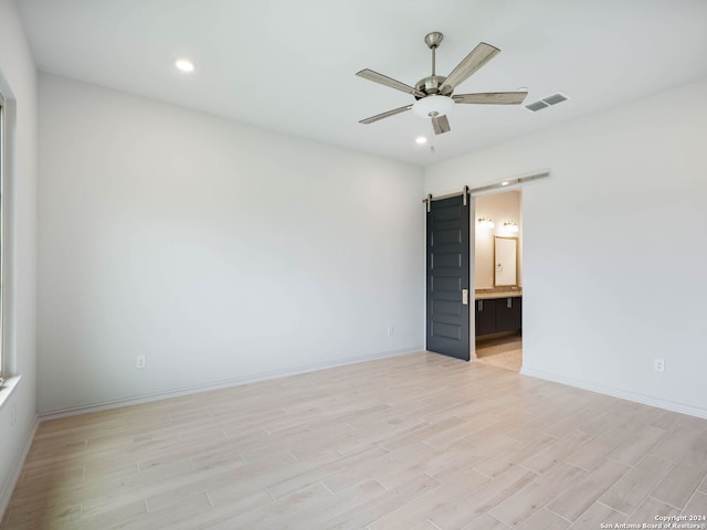 spare room with a barn door, ceiling fan, and light hardwood / wood-style floors