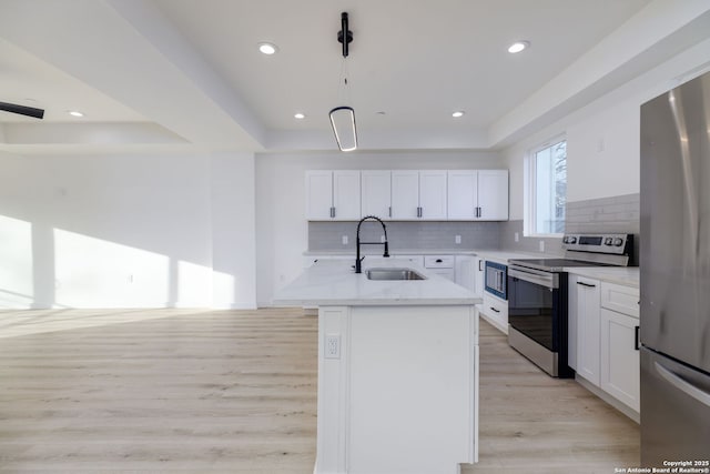 kitchen featuring sink, appliances with stainless steel finishes, a kitchen island with sink, white cabinetry, and a raised ceiling