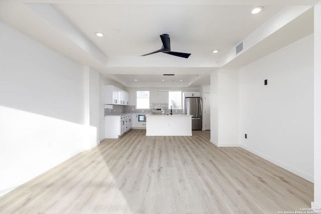 unfurnished living room with sink, a tray ceiling, ceiling fan, and light wood-type flooring