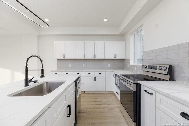 kitchen with stainless steel appliances, white cabinetry, sink, and light stone counters