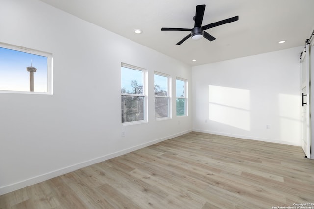 spare room featuring ceiling fan, a barn door, and light hardwood / wood-style floors