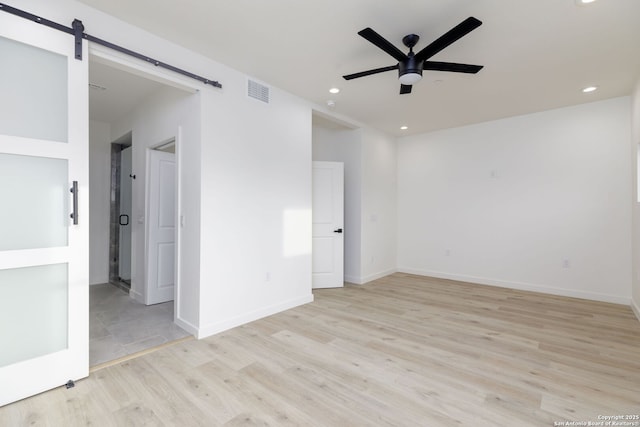 unfurnished room featuring light hardwood / wood-style flooring, a barn door, and ceiling fan