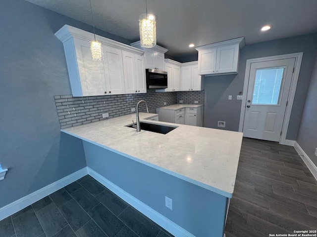 kitchen featuring sink, tasteful backsplash, hanging light fixtures, kitchen peninsula, and white cabinets