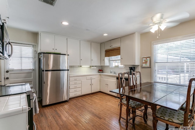 kitchen with appliances with stainless steel finishes, backsplash, tile counters, white cabinets, and light wood-type flooring