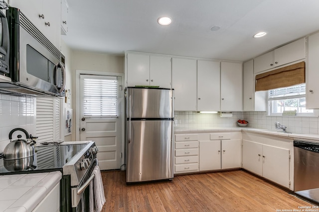 kitchen featuring sink, light hardwood / wood-style flooring, appliances with stainless steel finishes, backsplash, and white cabinets