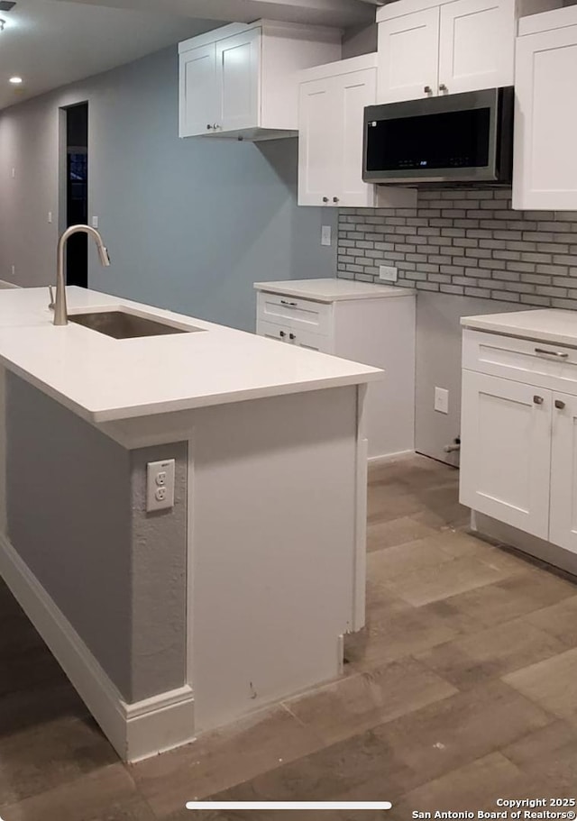 kitchen with sink, a center island with sink, light wood-type flooring, decorative backsplash, and white cabinets