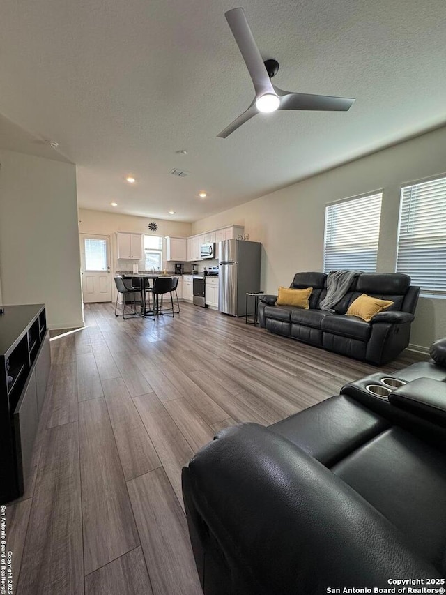 living room with ceiling fan, light hardwood / wood-style flooring, and a textured ceiling