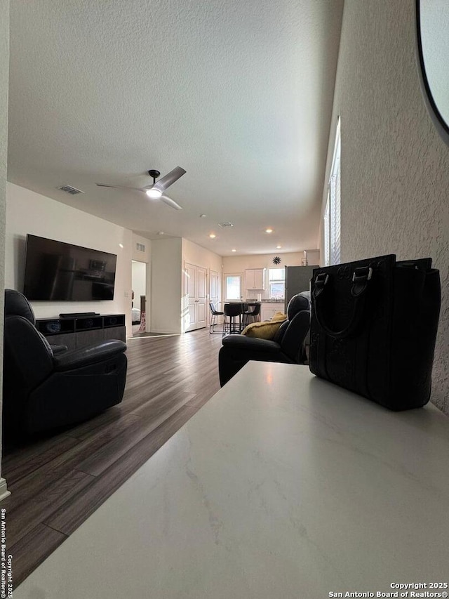 living room featuring ceiling fan, hardwood / wood-style flooring, and a textured ceiling