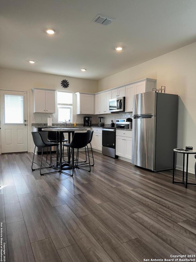 kitchen with white cabinetry, dark wood-type flooring, a breakfast bar area, and appliances with stainless steel finishes